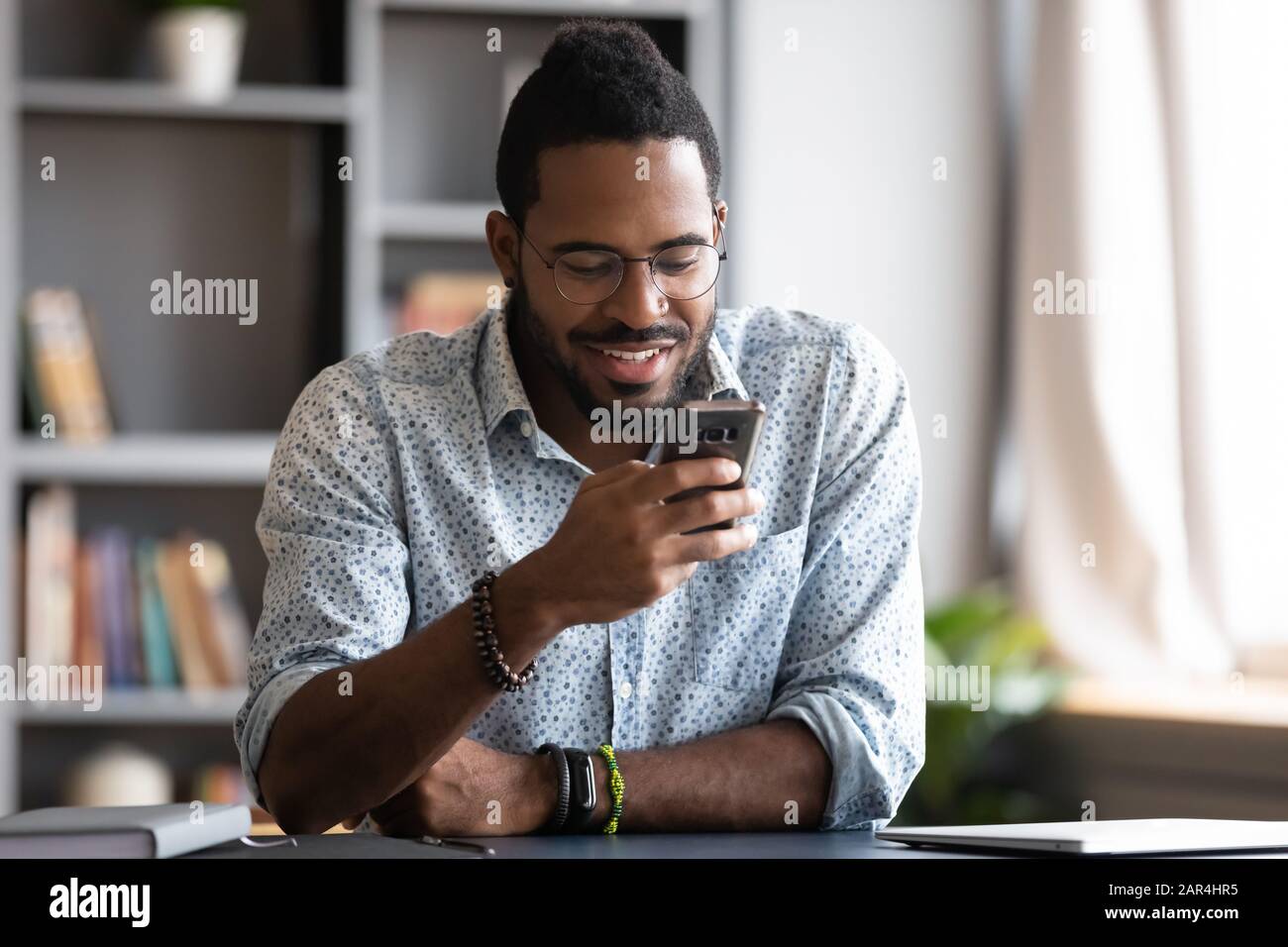 Happy african man using smartphone sit at home office desk Stock Photo