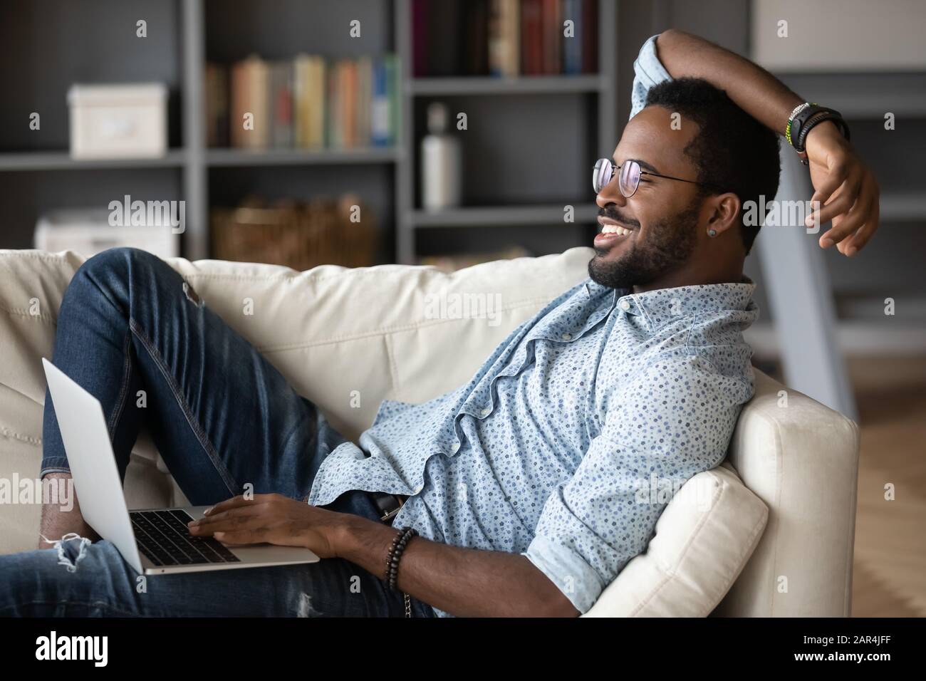 Relaxed african man resting on couch using laptop at home Stock Photo