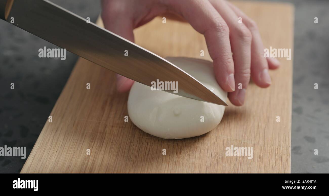 Closeup man slicing fresh mozzarella on oak board, wide photo Stock