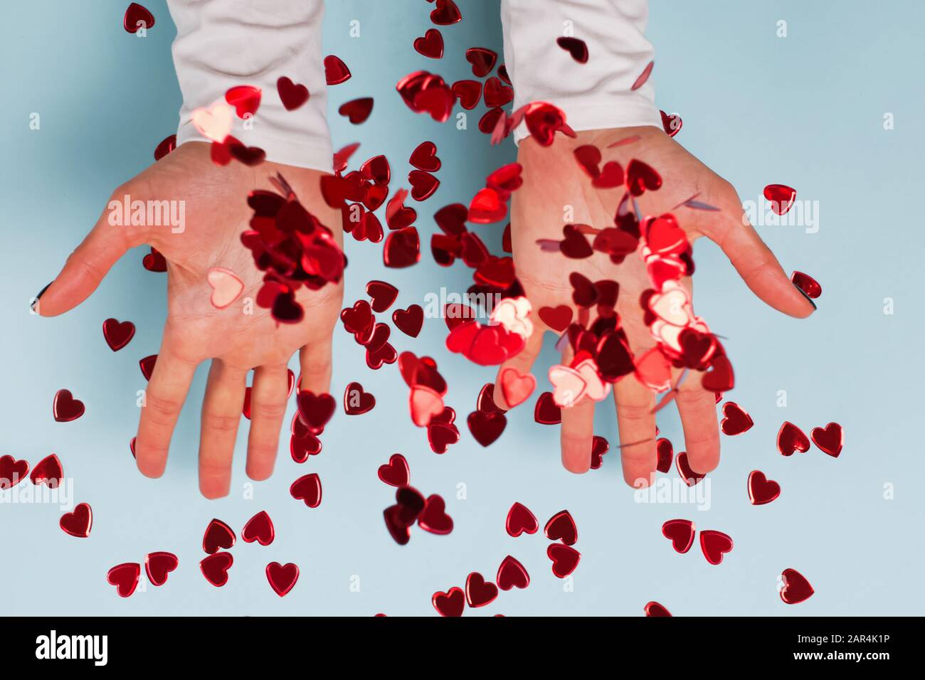 Woman's hands throwing up red heart shaped glitter confetti on blue