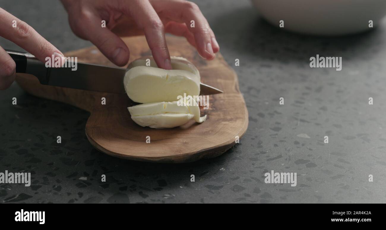 Closeup man slicing fresh mozzarella on olive board, wide photo Stock