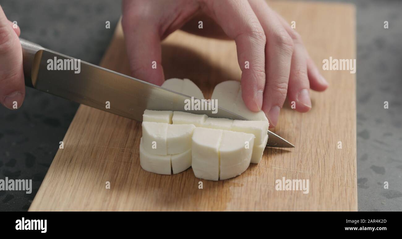 Closeup man slicing fresh mozzarella on oak board, wide photo Stock