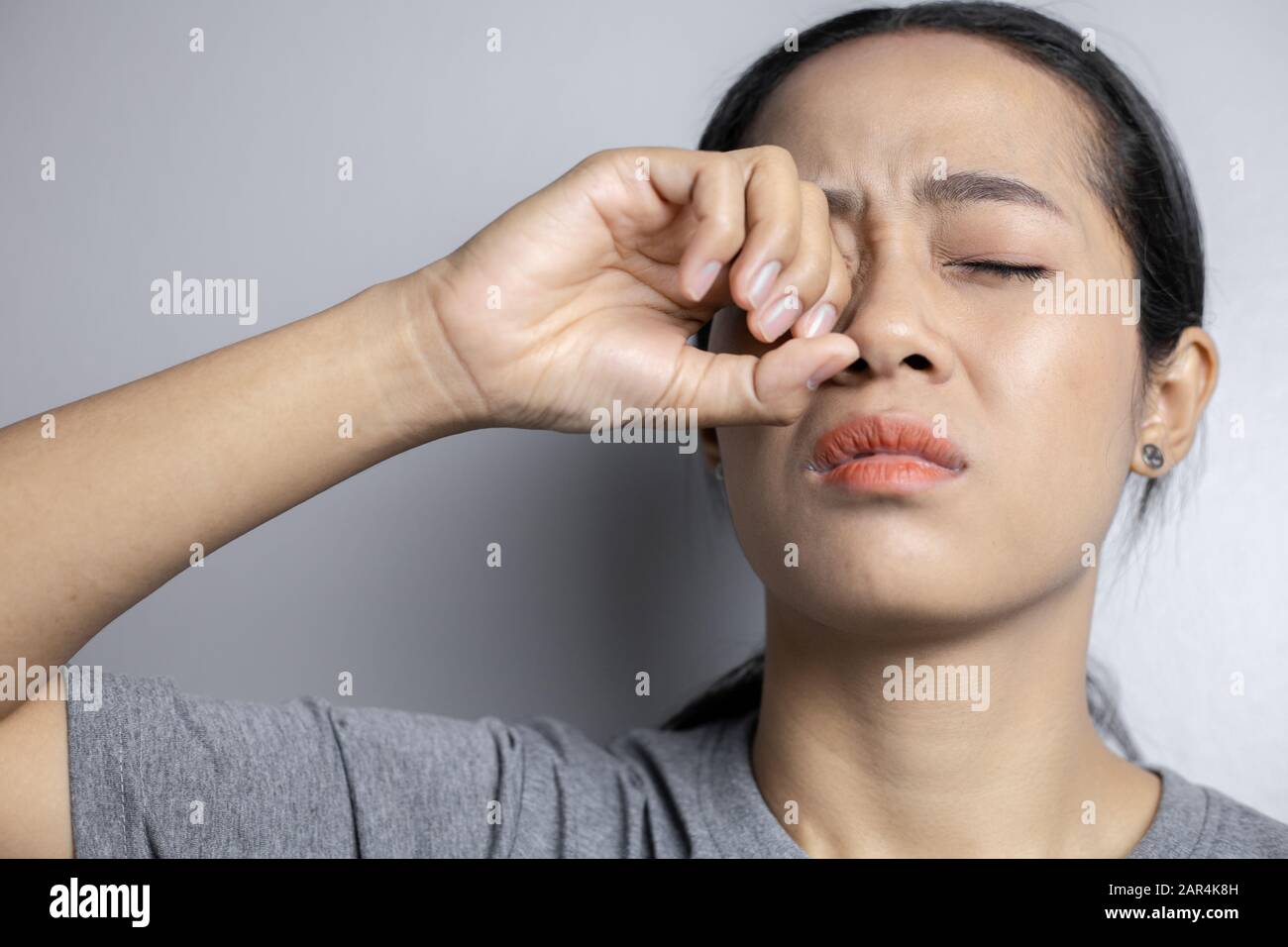 Young woman with of eye pain on a gray background. Asian woman is