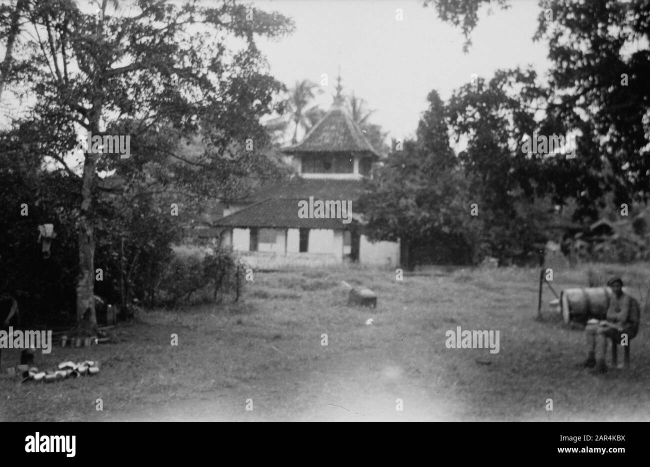 Visit of the Chief Army chaplain H.J.J.M. van Straelen to Semarang  An outpost? A soldier on the left is sitting on some sort of chair. In the middle a church or a mosque. Left are cans Date: February 1947 Location: Indonesia, Dutch East Indies, Semarang Stock Photo