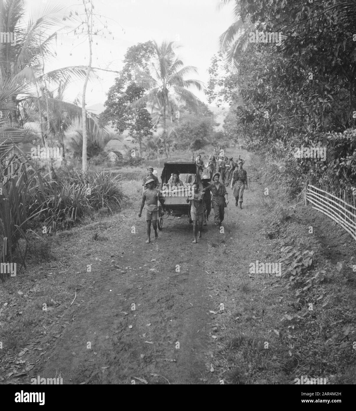 A patrol runs behind a dokar pulled by two men. Inside the cart are an old man and woman Date: September 1947 Location: Indonesia, Dutch East Indies Stock Photo