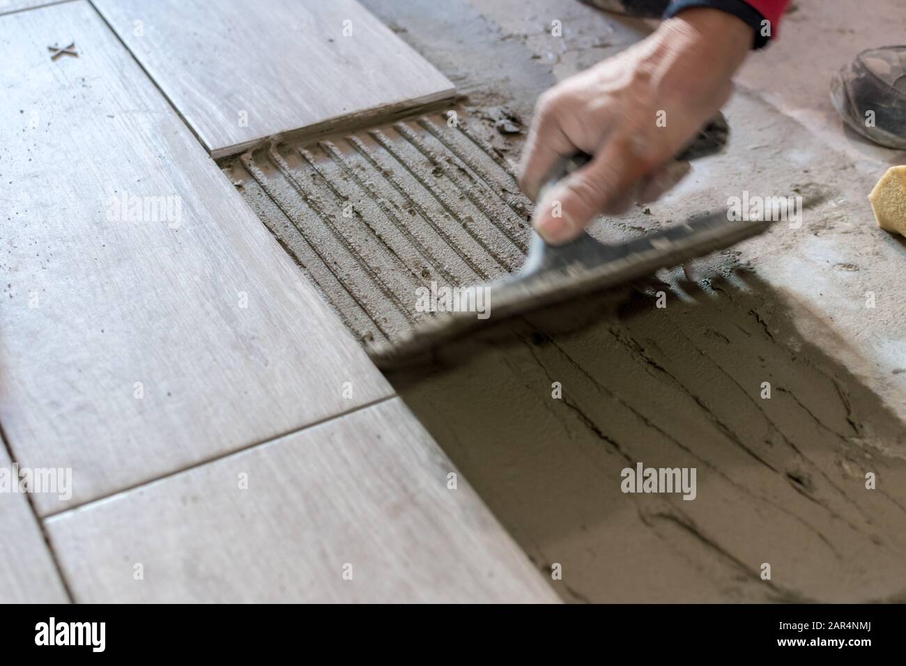 Man installing rectangular shaped floor tiles in kitchen. Applying adhesive before installation and verifying afterwards Stock Photo