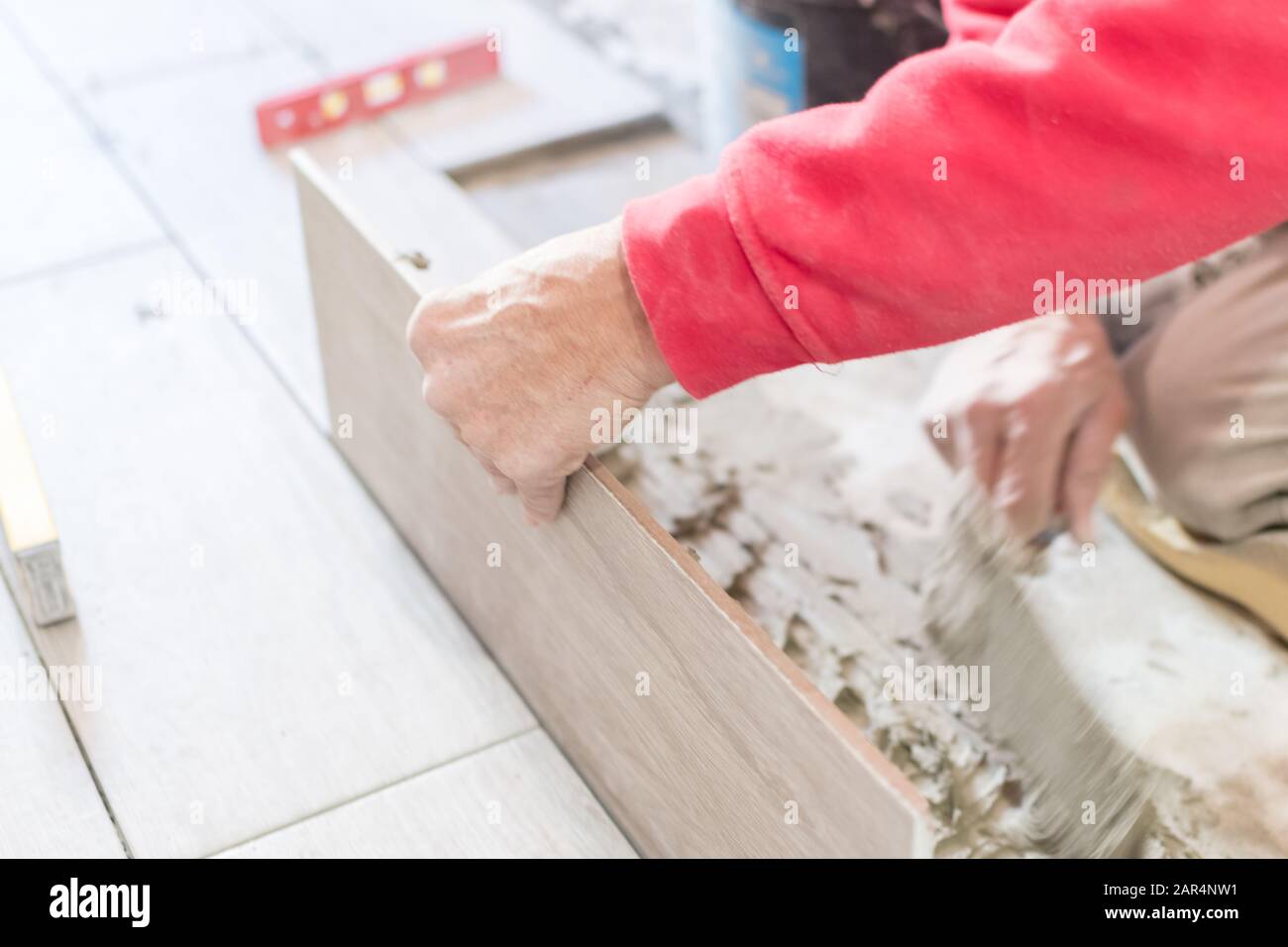 Man installing rectangular shaped floor tiles in kitchen. Applying adhesive before installation and verifying afterwards Stock Photo