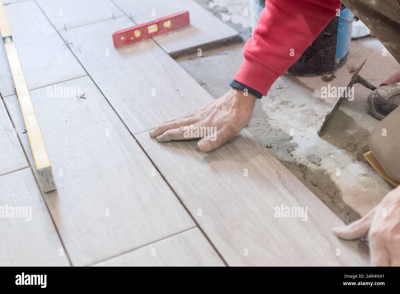 Man installing rectangular shaped floor tiles in kitchen. Applying adhesive before installation and verifying afterwards Stock Photo