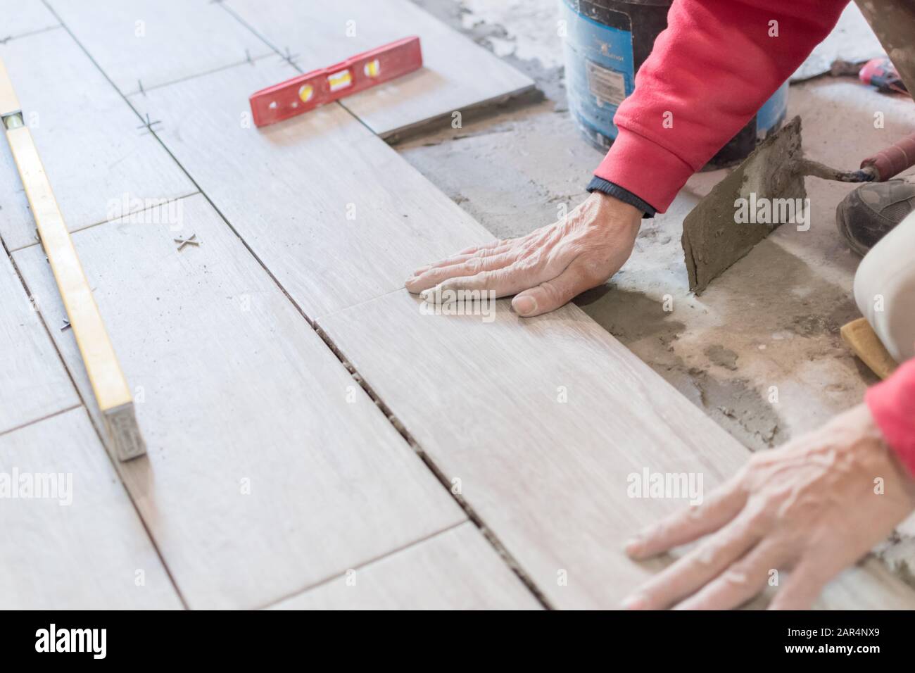 Man installing rectangular shaped floor tiles in kitchen. Applying adhesive before installation and verifying afterwards Stock Photo