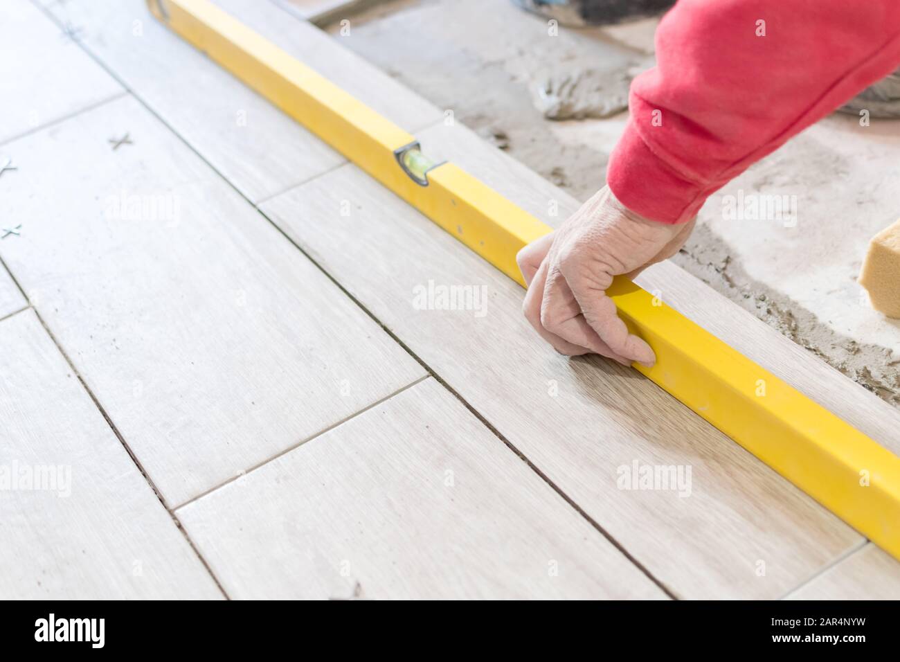 Man installing rectangular shaped floor tiles in kitchen. Applying adhesive before installation and verifying afterwards Stock Photo