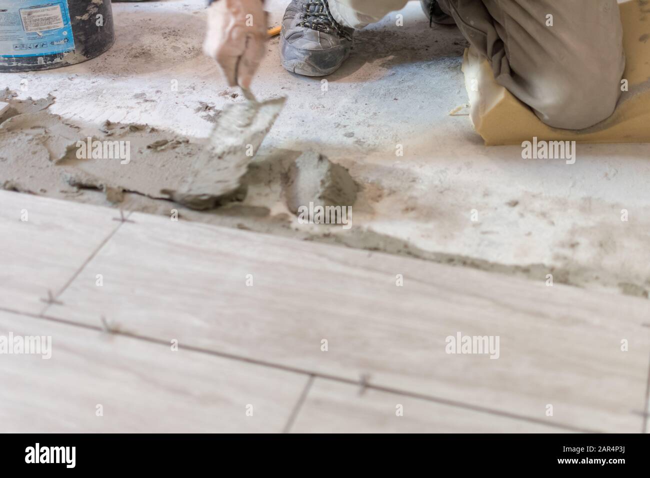 Man installing rectangular shaped floor tiles in kitchen. Applying ...