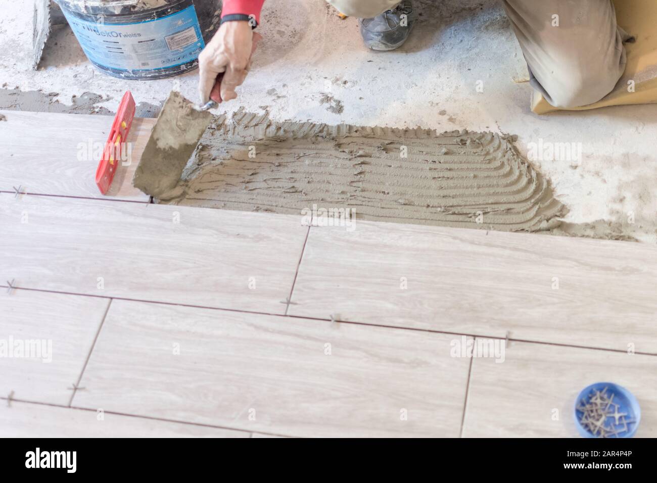 Man installing rectangular shaped floor tiles in kitchen. Applying ...