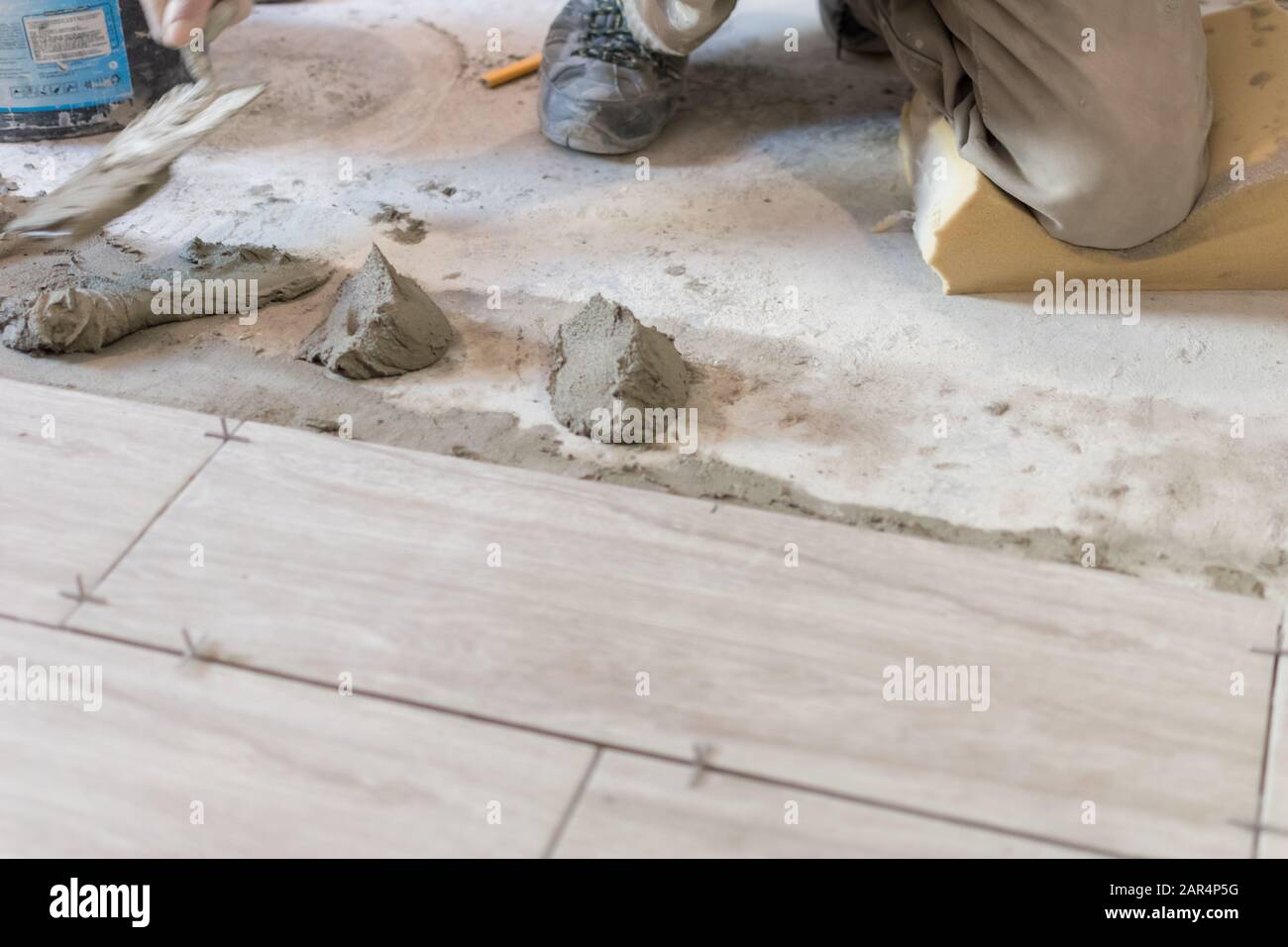 Man installing rectangular shaped floor tiles in kitchen. Applying adhesive before installation and verifying afterwards Stock Photo