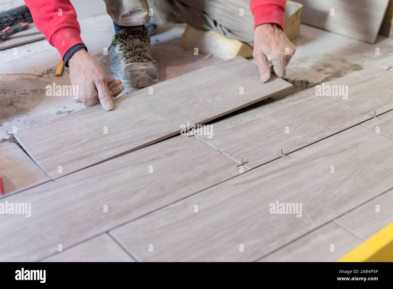 Man installing rectangular shaped floor tiles in kitchen. Applying adhesive before installation and verifying afterwards Stock Photo