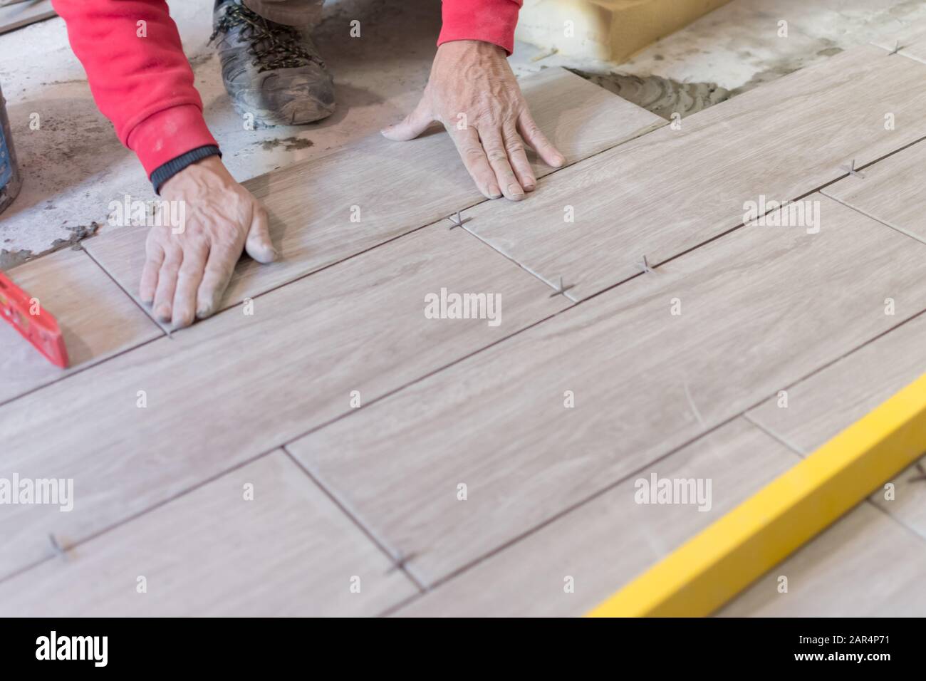 Man installing rectangular shaped floor tiles in kitchen. Applying adhesive before installation and verifying afterwards Stock Photo