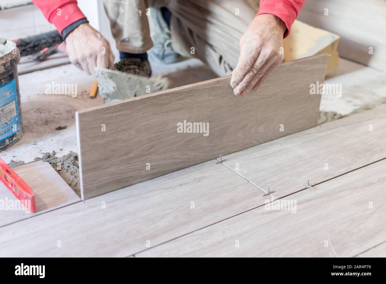 Man installing rectangular shaped floor tiles in kitchen. Applying adhesive before installation and verifying afterwards Stock Photo