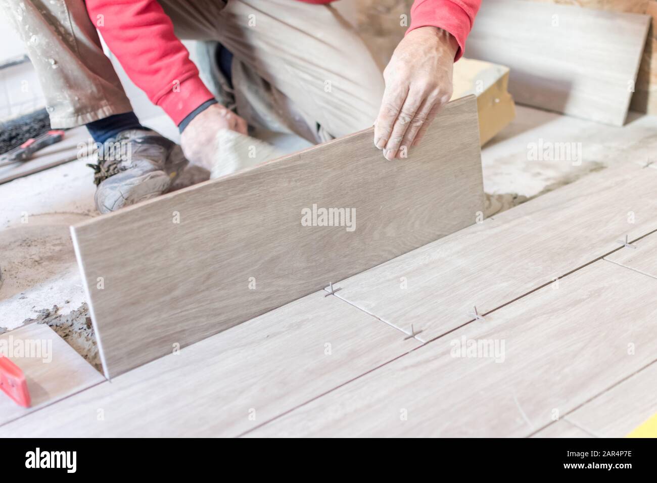 Man installing rectangular shaped floor tiles in kitchen. Applying adhesive before installation and verifying afterwards Stock Photo