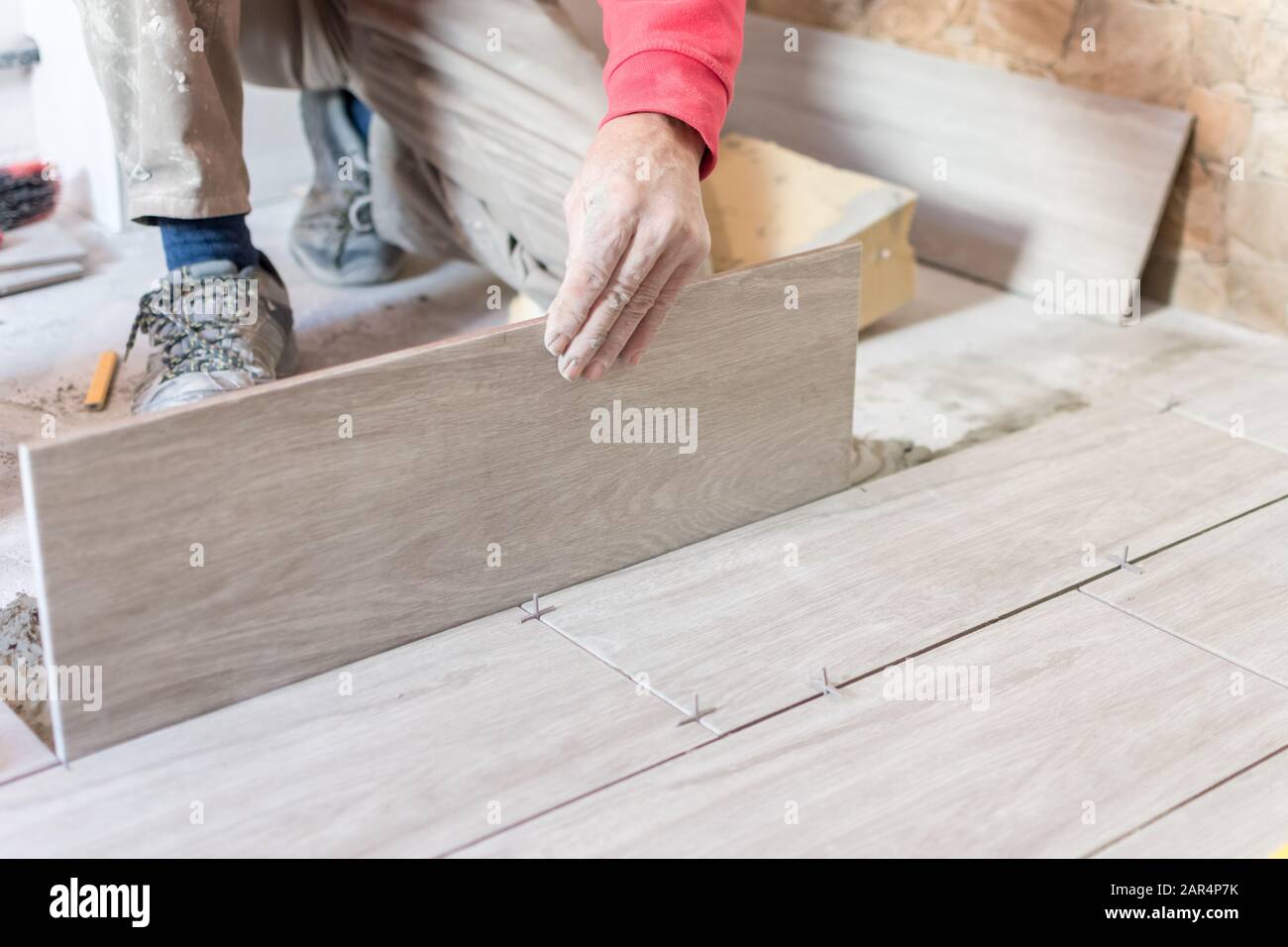 Man installing rectangular shaped floor tiles in kitchen. Applying adhesive before installation and verifying afterwards Stock Photo