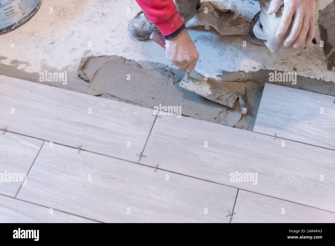 Man installing rectangular shaped floor tiles in kitchen. Applying ...