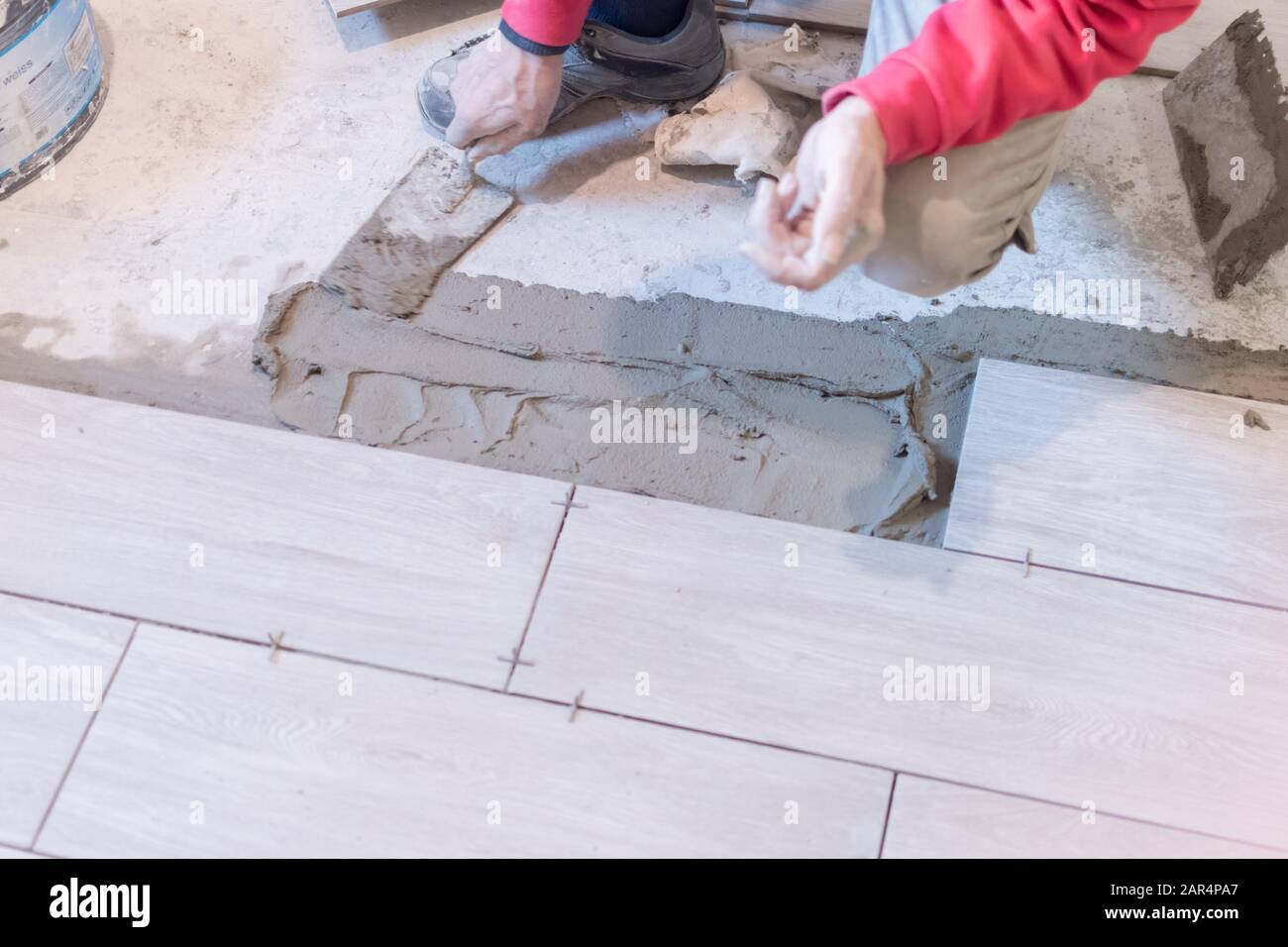 Man installing rectangular shaped floor tiles in kitchen. Applying adhesive before installation and verifying afterwards Stock Photo