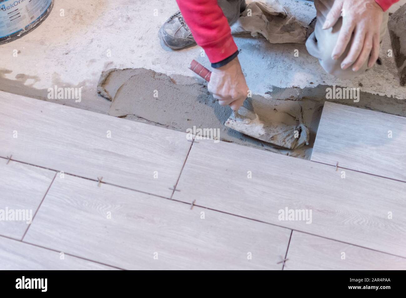 Man installing rectangular shaped floor tiles in kitchen. Applying adhesive before installation and verifying afterwards Stock Photo
