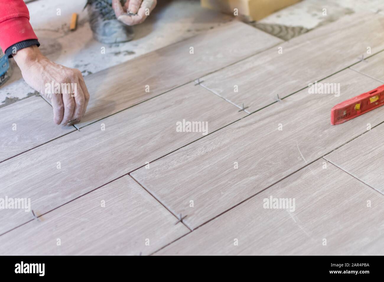 Man installing rectangular shaped floor tiles in kitchen. Applying adhesive before installation and verifying afterwards Stock Photo