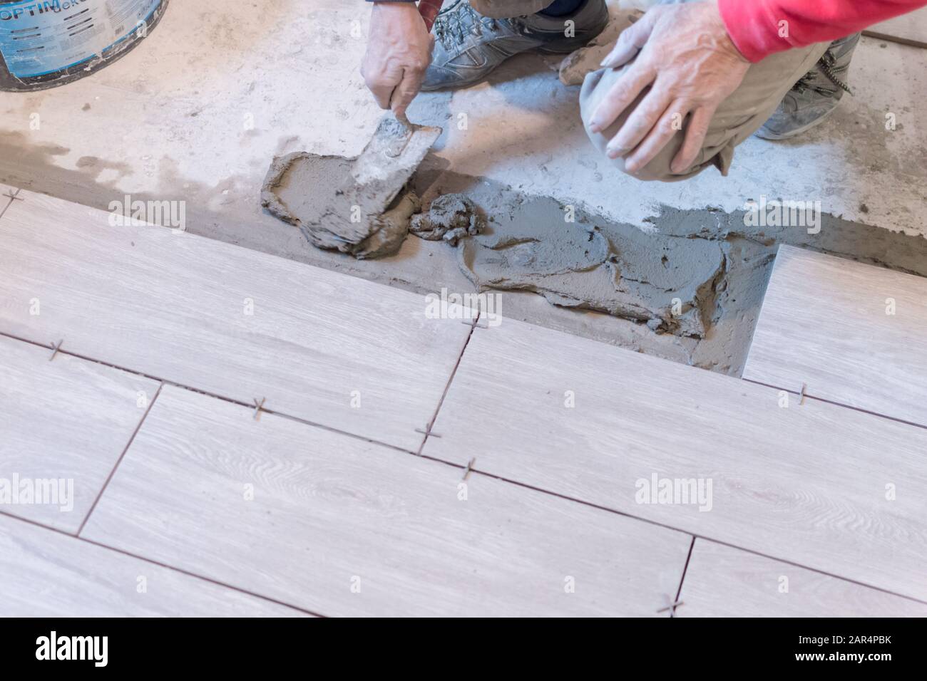 Man installing rectangular shaped floor tiles in kitchen. Applying adhesive before installation and verifying afterwards Stock Photo