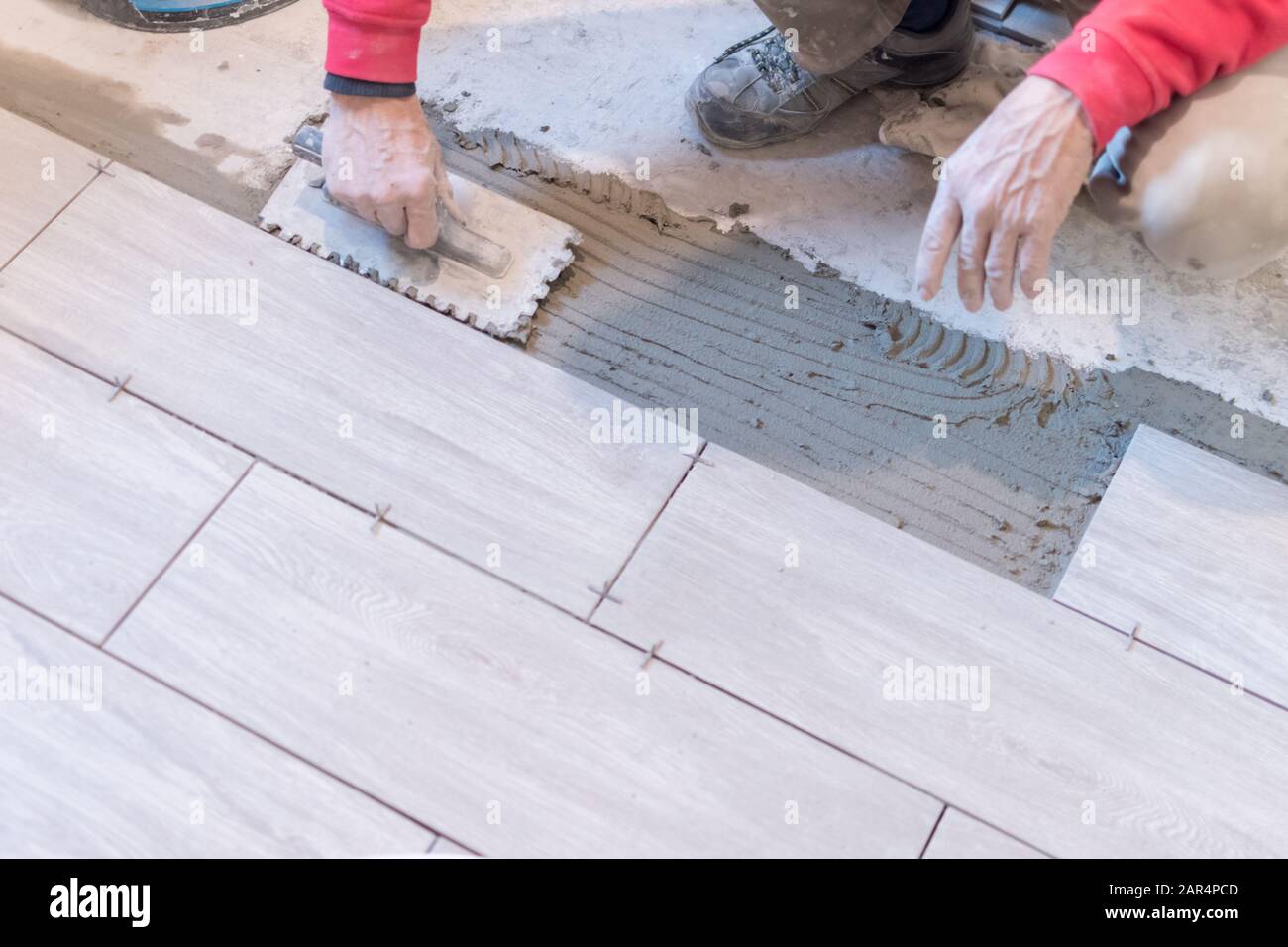 Man installing rectangular shaped floor tiles in kitchen. Applying adhesive before installation and verifying afterwards Stock Photo
