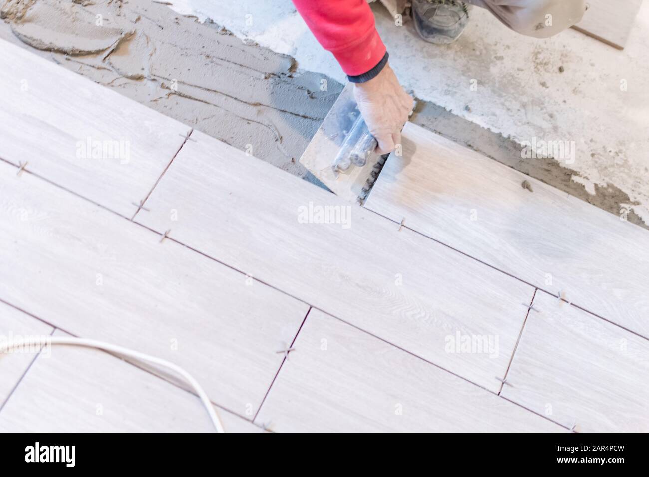 Man installing rectangular shaped floor tiles in kitchen. Applying adhesive before installation and verifying afterwards Stock Photo
