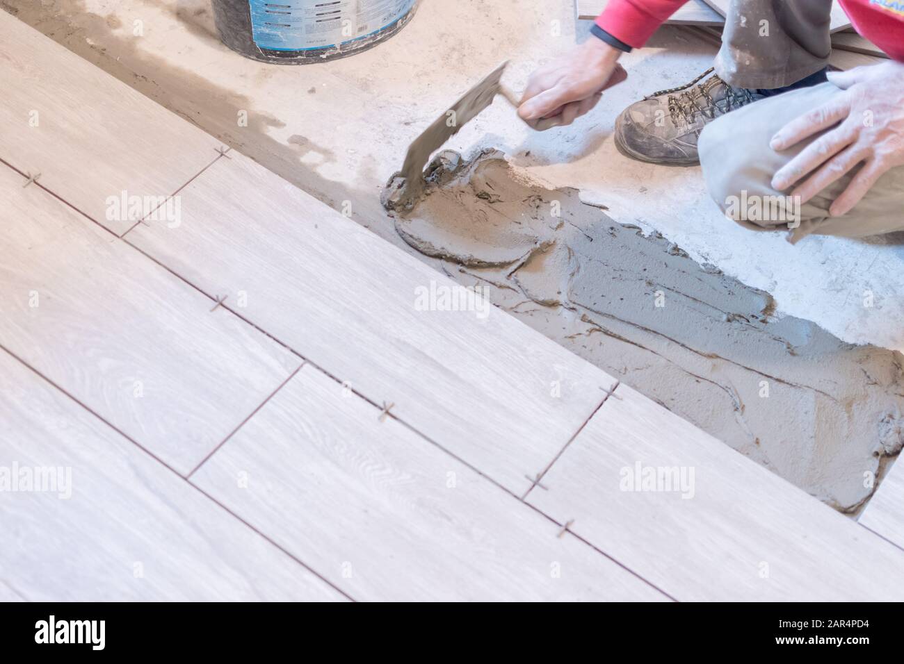 Man installing rectangular shaped floor tiles in kitchen. Applying ...