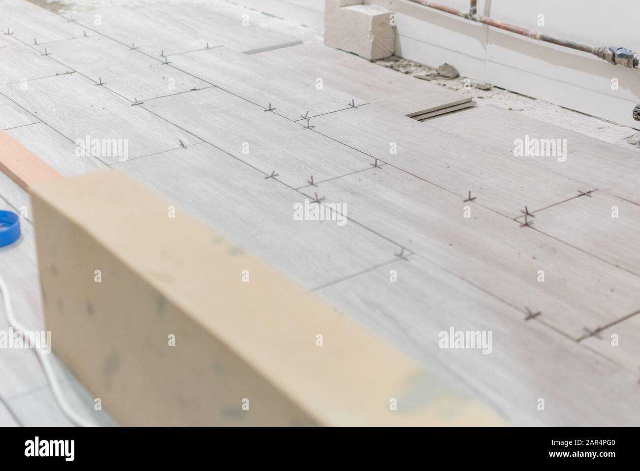 Man installing rectangular shaped floor tiles in kitchen. Applying adhesive before installation and verifying afterwards Stock Photo