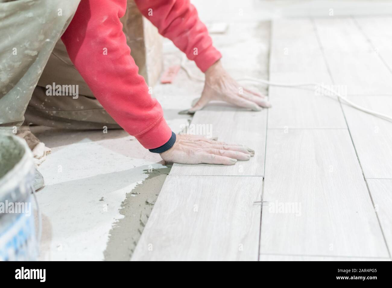 Man installing rectangular shaped floor tiles in kitchen. Applying ...