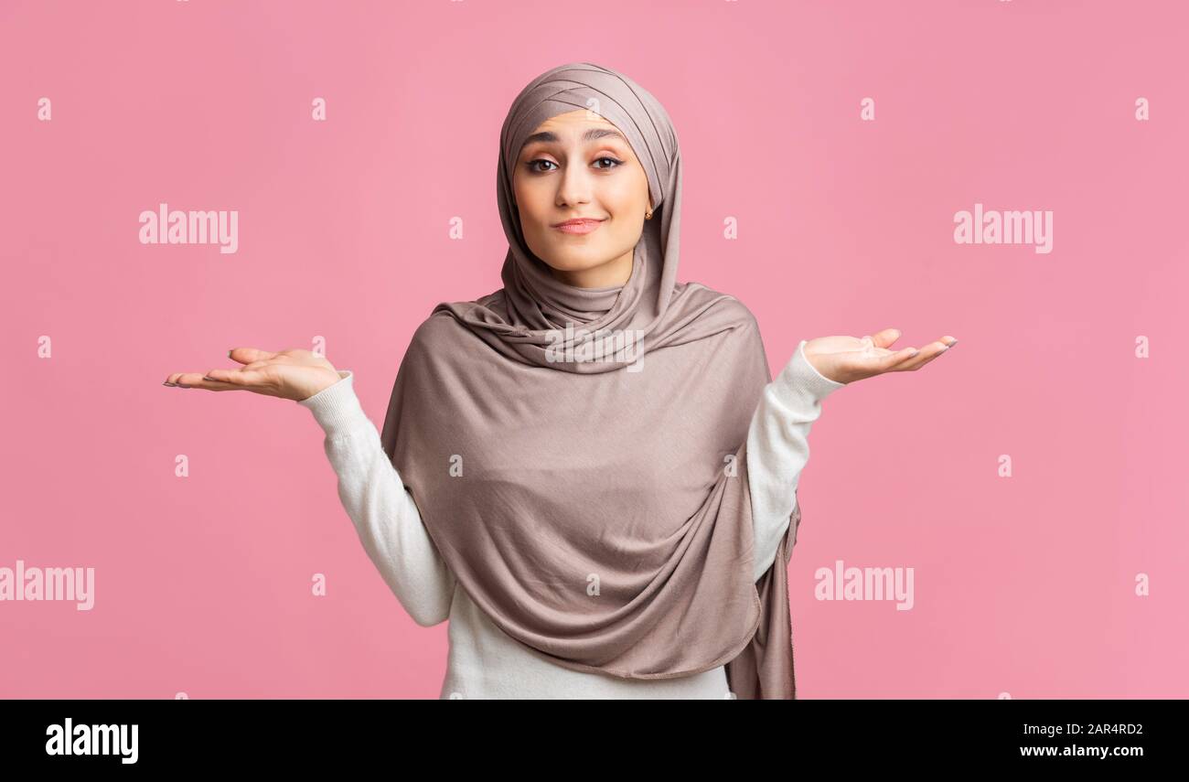Unsure Muslim Woman In Hijab Shrugging Shoulders On Pink Studio Background Stock Photo