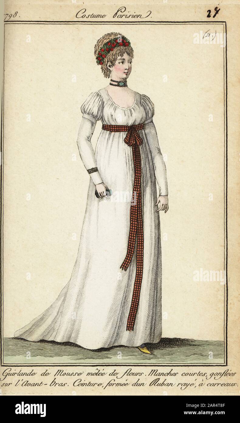 Woman in the fashions of 1798 with short hair under a garland. She wears a  short victim hairstyle under a garland of moss and flowers. Her white tunic  dress has short sleeves