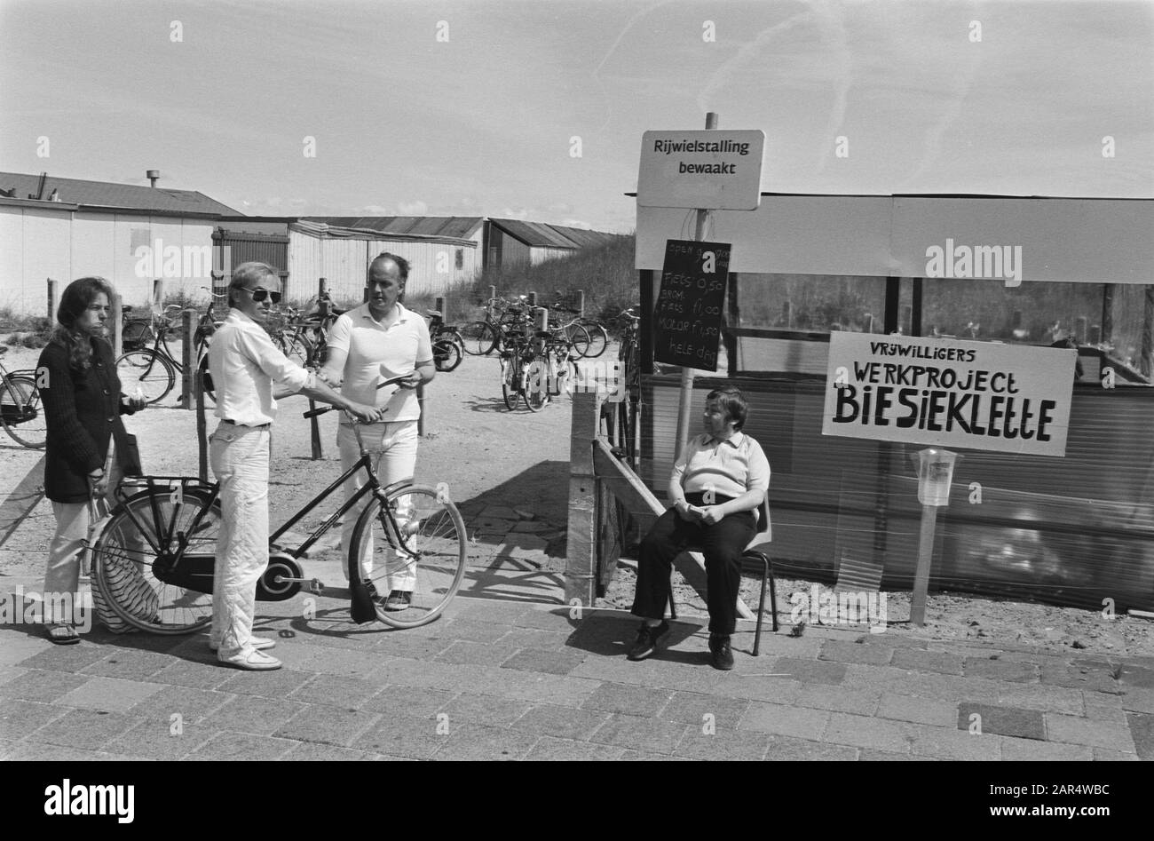 Bicycle parking staffed by unemployed persons, with retention of benefit in Scheveningen  Cyclist at the parking with the sign Volunteers work project Biesieklette Date: 20 July 1983 Location: Scheveningen, South Holland Keywords: bicycle parking, volunteers, unemployment Stock Photo