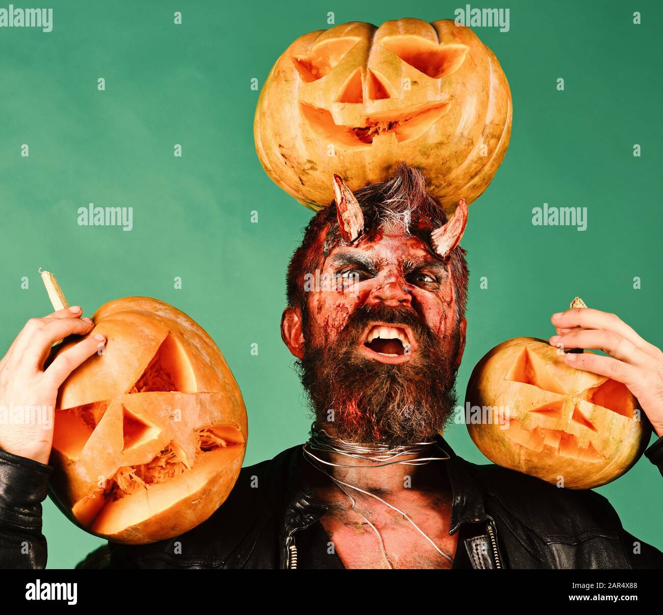 Demon with horns and mad face holds jack o Man wearing scary with Halloween pumpkins and bats decor on background. Halloween costume party concept. Devil or monster makes decorations Stock Photo - Alamy
