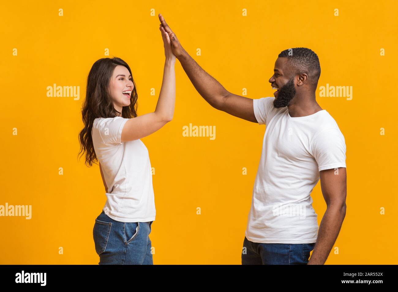 Joyful interracial sweethearts giving high-five to each other, clapping hands Stock Photo