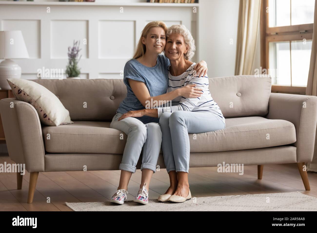 Portrait of smiling young blonde woman cuddling senior old mother. Stock Photo