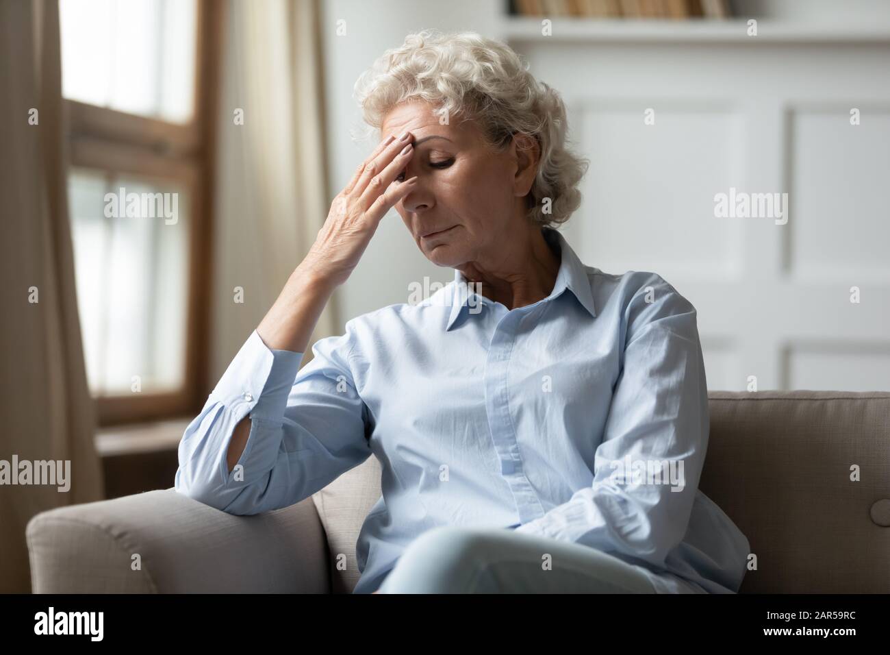 Frustrated nervous middle aged hoary woman touching forehead. Stock Photo