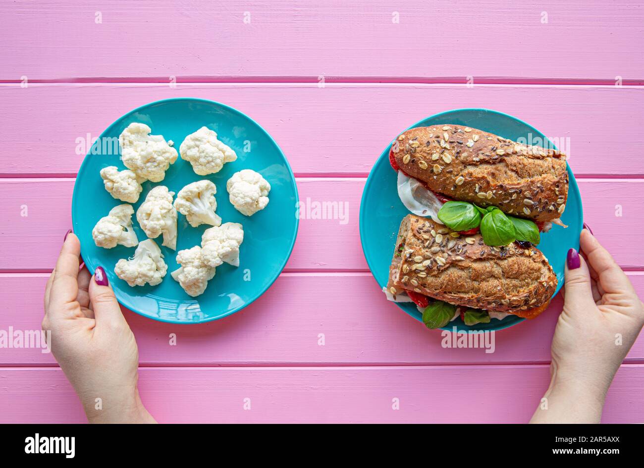 Female hands holding two plates and choosing food to eat between vegetables or sandwich, diet concept. Stock Photo