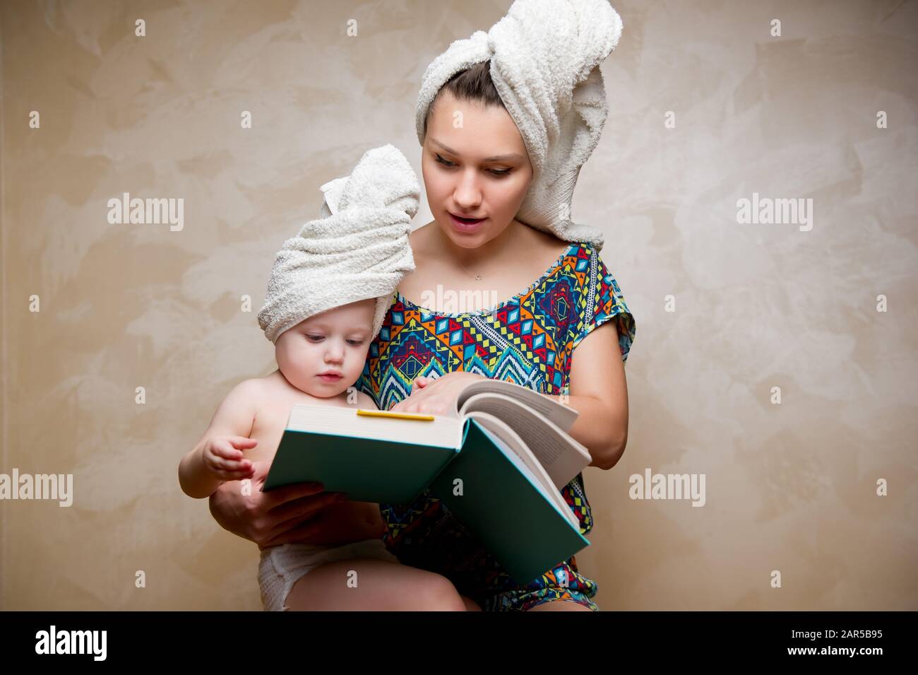mom and daughter read a book after bath with towels on their heads Stock Photo