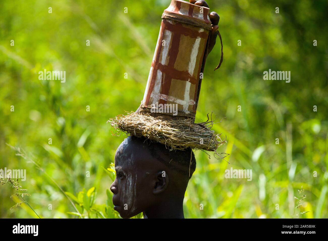 Mursi boy carrying a jar on his head. The Mursi (or Murzu) are a Sub-Saharan African nomadic cattle herder tribe located in the Omo valley in southwes Stock Photo
