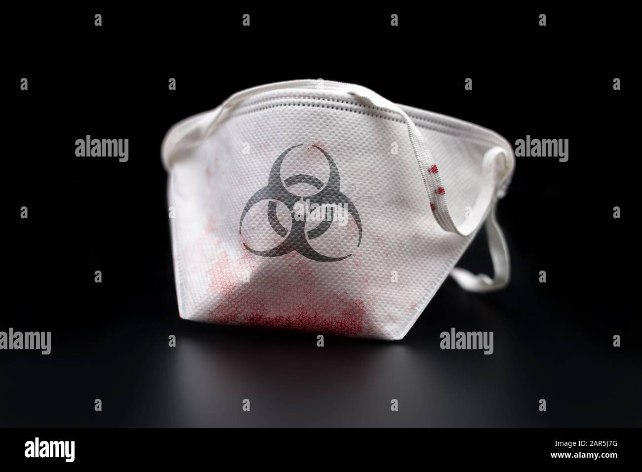 Blood-stained safety mask with a biohazard symbol on it, aftermath of a biological infection (isolated on a black background). Stock Photo