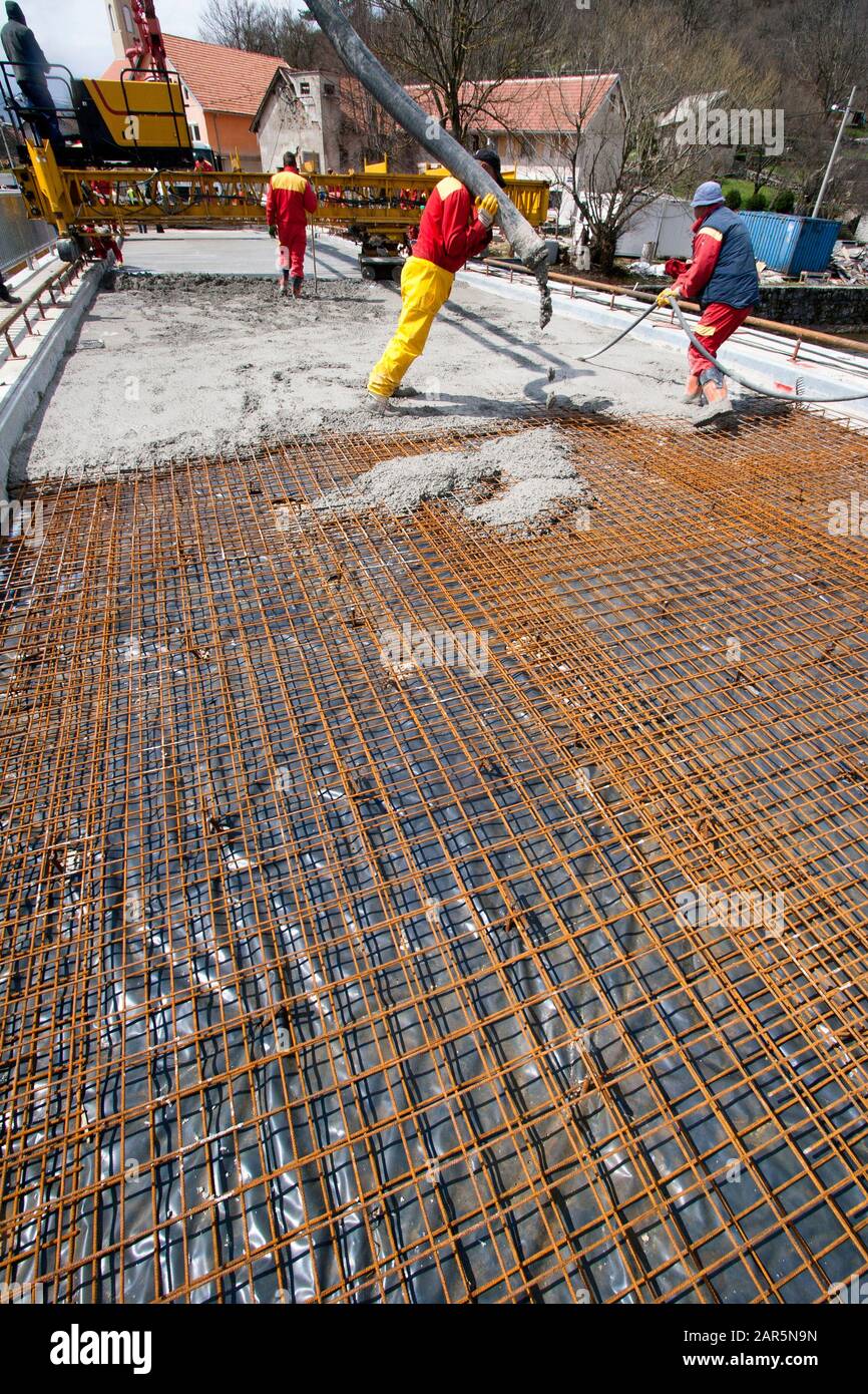 Group of construction workers spreading freshly poured concrete mix on the bridge Stock Photo