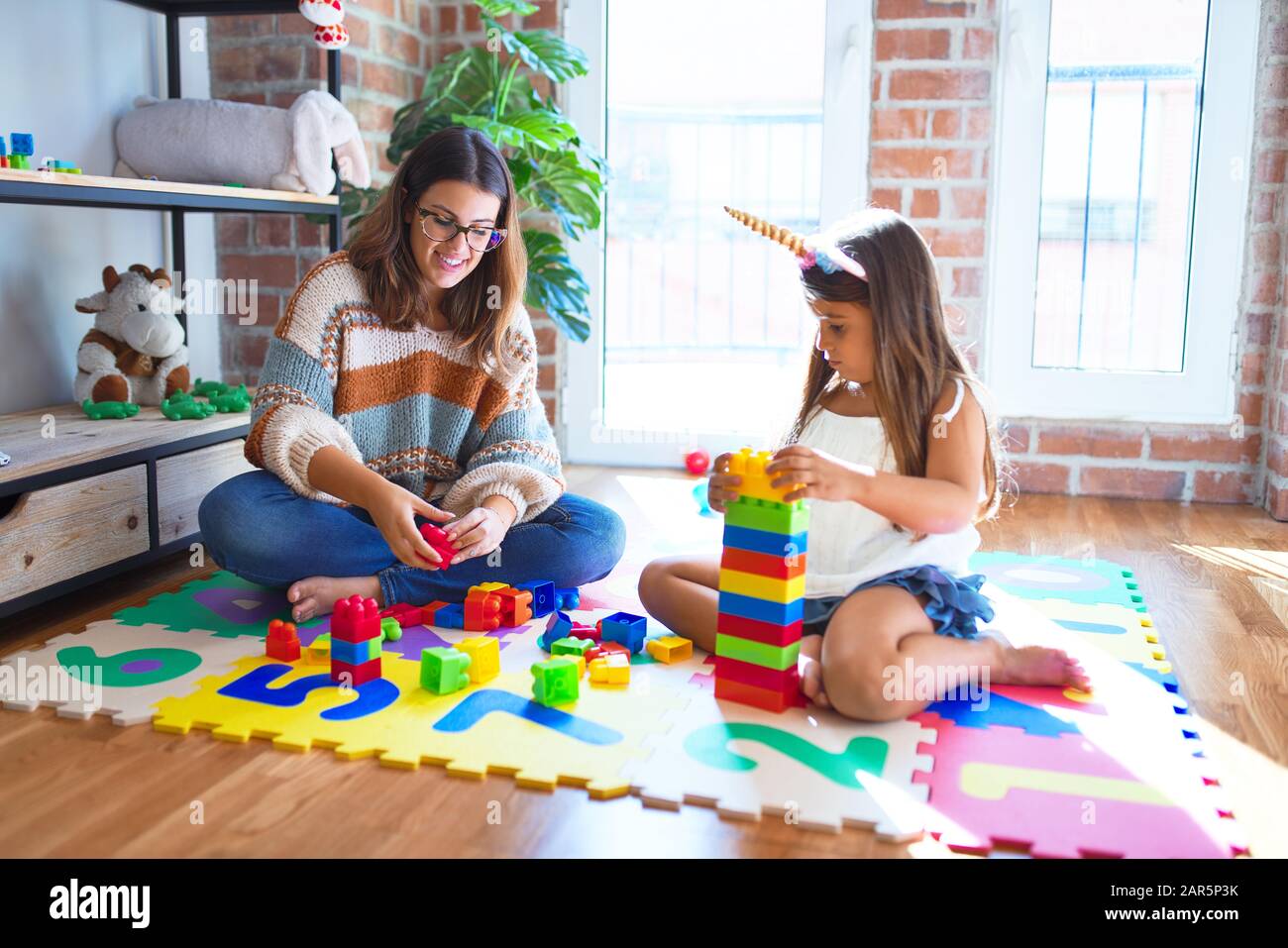Beautiful teacher and toddler playing with building blocks toy around