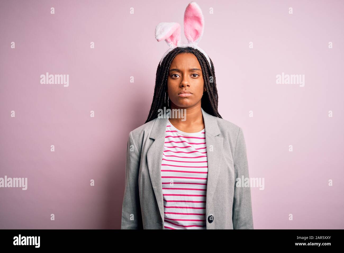 Young african american girl wearing cute easter bunny ears over pink  background with serious expression on face. Simple and natural looking at  the cam Stock Photo - Alamy