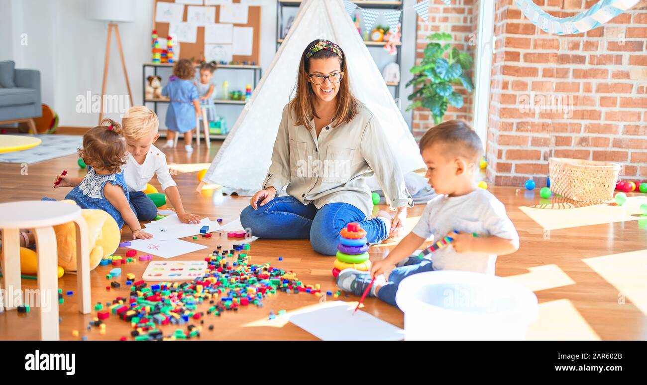 Beautiful teacher and group of toddlers playing around lots of toys at