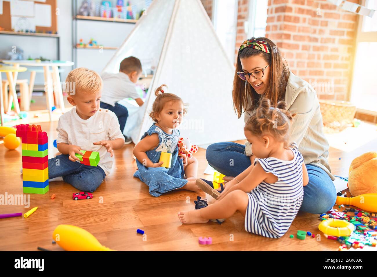 Beautiful teacher and group of toddlers playing around lots of toys at