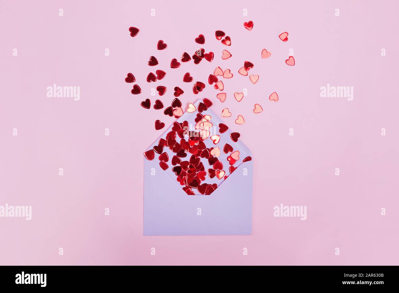 Small red shiny hearts with envelope on pink background Stock Photo