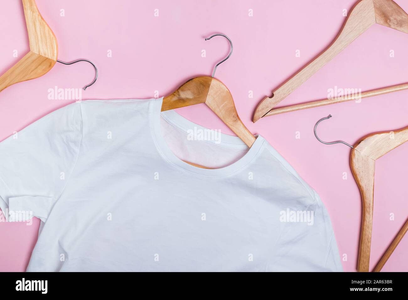 White T-Shirts on wooden hangers over pink background Stock Photo